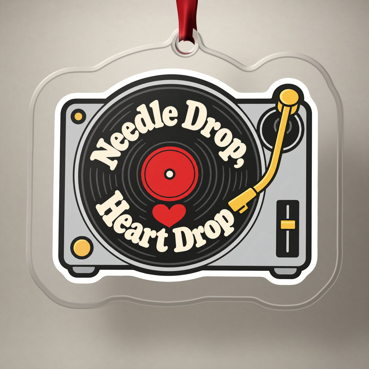 Needle Drop, Heart Drop Turntable clear acrylic Christmas ornament on a plain studio backdrop with its red ribbon