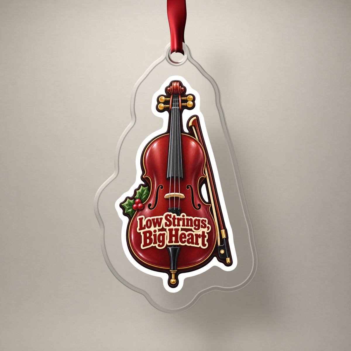 Low Strings, Big Heart Cello clear acrylic Christmas ornament on a plain studio backdrop with its red ribbon