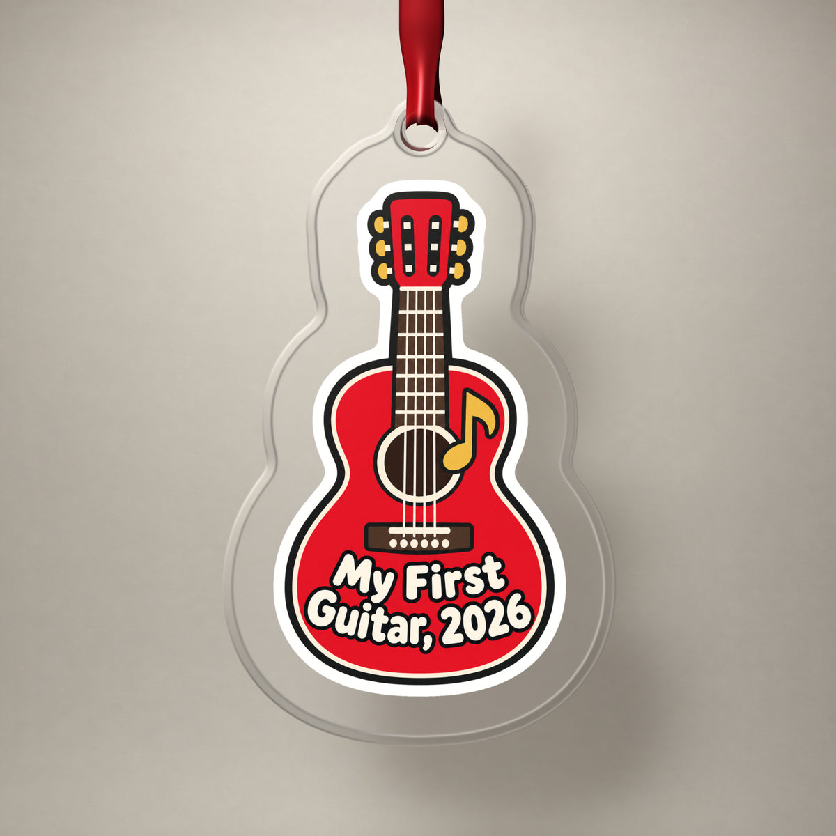 My First Guitar 2026 clear acrylic Christmas ornament on a plain studio backdrop with its red ribbon
