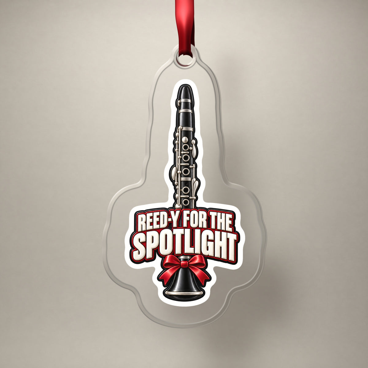 Reed-y for the Spotlight Clarinet clear acrylic Christmas ornament on a plain studio backdrop with its red ribbon