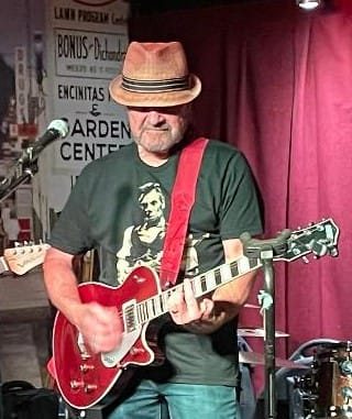 Kenneth S. on stage in the dark Lincoln Guitar tee, playing a red electric guitar