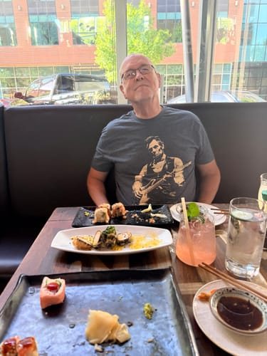 David H. at a restaurant table in the grey Lincoln Guitar tee