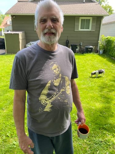 Margaret W.’s photo of a man holding a coffee cup in the grey Lincoln Guitar tee