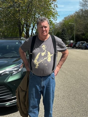 Jan P.'s photo of her husband in suspenders wearing the grey Lincoln Guitar tee
